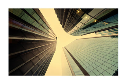 A low-angle photograph of modern skyscrapers with glass and dark metal facades converging toward the sky, presented with a white border.