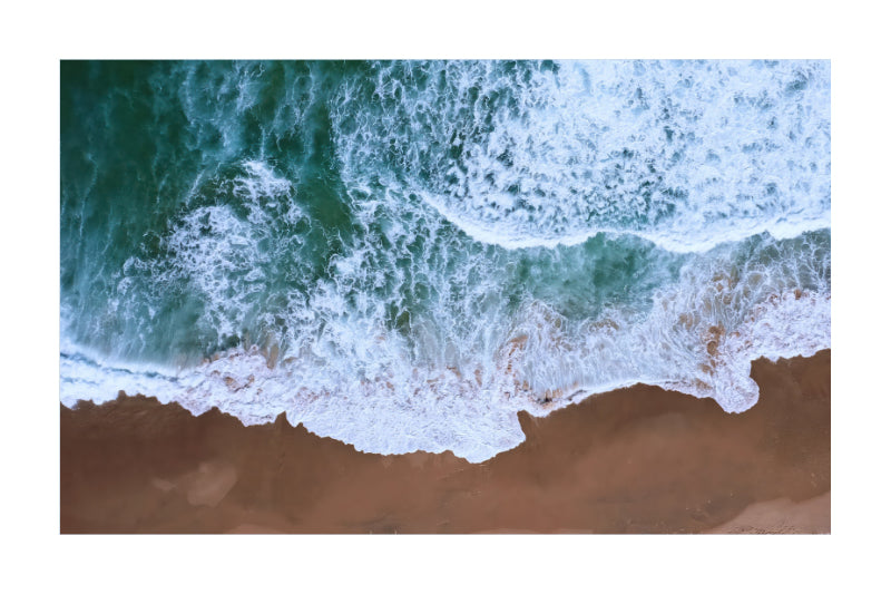 An aerial view of ocean waves with white foam crashing onto a sandy beach, shown as a square print centered on a white background.