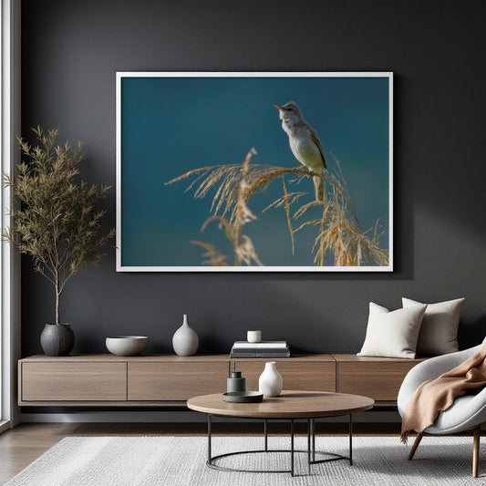 A large framed wall art print showing a small bird perched on dried grass against a deep blue background, displayed above a wooden console in a modern living room setting.
