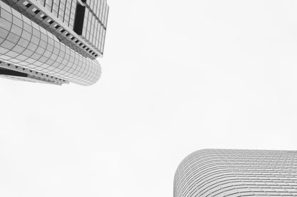 Black and white architectural photograph showing curved modern skyscrapers against a bright white sky, with large negative space in the center.