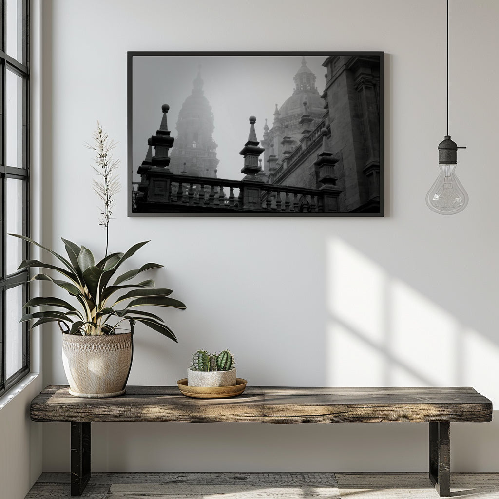 A black and white framed art print depicting historic architectural domes and spires, displayed on a white wall above a rustic wooden bench with a potted plant and a hanging light bulb in a modern room setting.