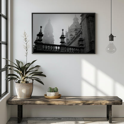 A black and white framed art print depicting historic architectural domes and spires, displayed on a white wall above a rustic wooden bench with a potted plant and a hanging light bulb in a modern room setting.