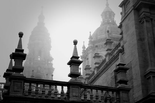 Black and white architectural photograph of domed historic buildings shrouded in mist, framed by a stone balustrade in the foreground.