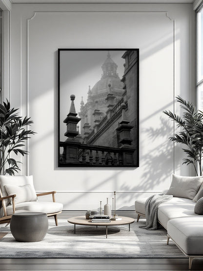 A black and white framed art print of a grand domed building, displayed on a white wall in a modern, sunlit living room with a sofa, armchair, and coffee table.