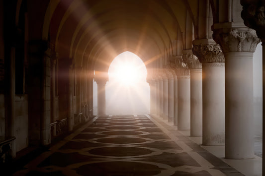 A scenic photograph of a grand stone colonnade with arches and columns, looking toward a bright sunburst opening at the end of the hall.
