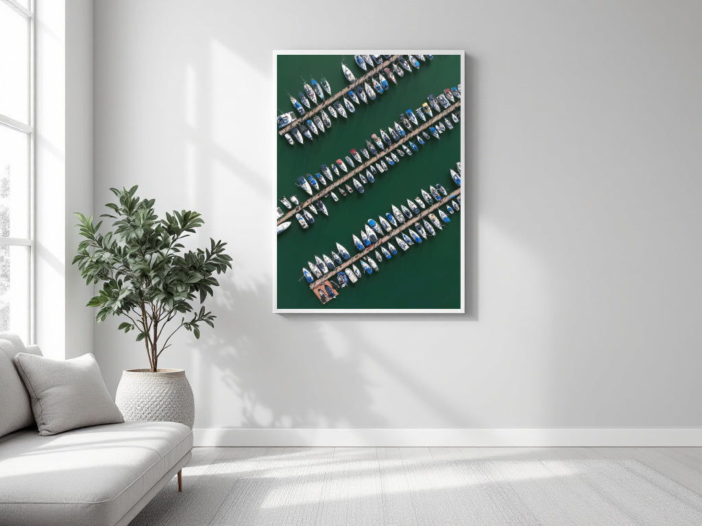 A framed aerial photograph of a marina with rows of boats on a dark green water background, displayed on a light gray wall in a modern living room setting next to a sofa and a potted plant.