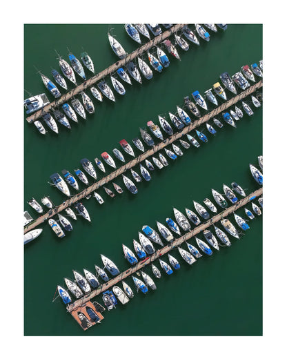 Aerial view of multiple sailboats moored along diagonal docks over deep green water.