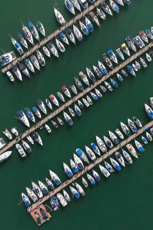 Aerial view of many small boats tied to parallel docks in a marina on deep green water.