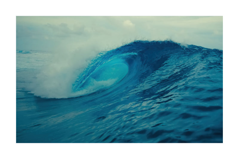 A square art print depicting a powerful blue ocean wave curling under a cloudy sky, presented with a white border.