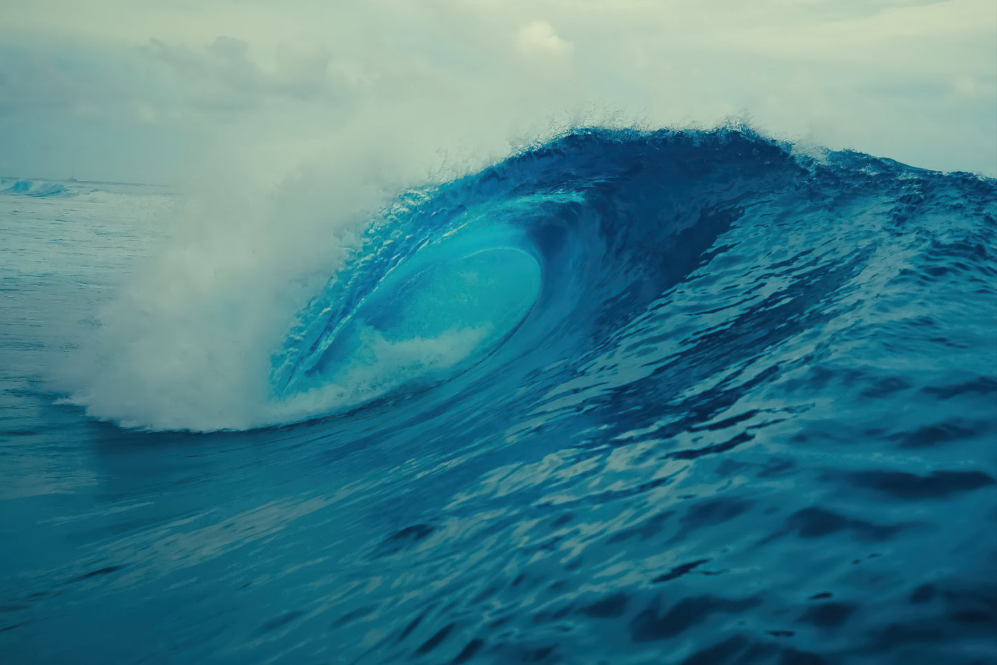 A dramatic blue ocean wave curls into a barrel with white foam at the crest under an overcast sky.