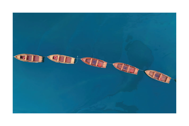 Aerial view of five small wooden boats tied in a line across deep blue water.