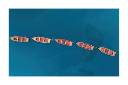 Aerial view of five small wooden boats tied in a line across deep blue water.