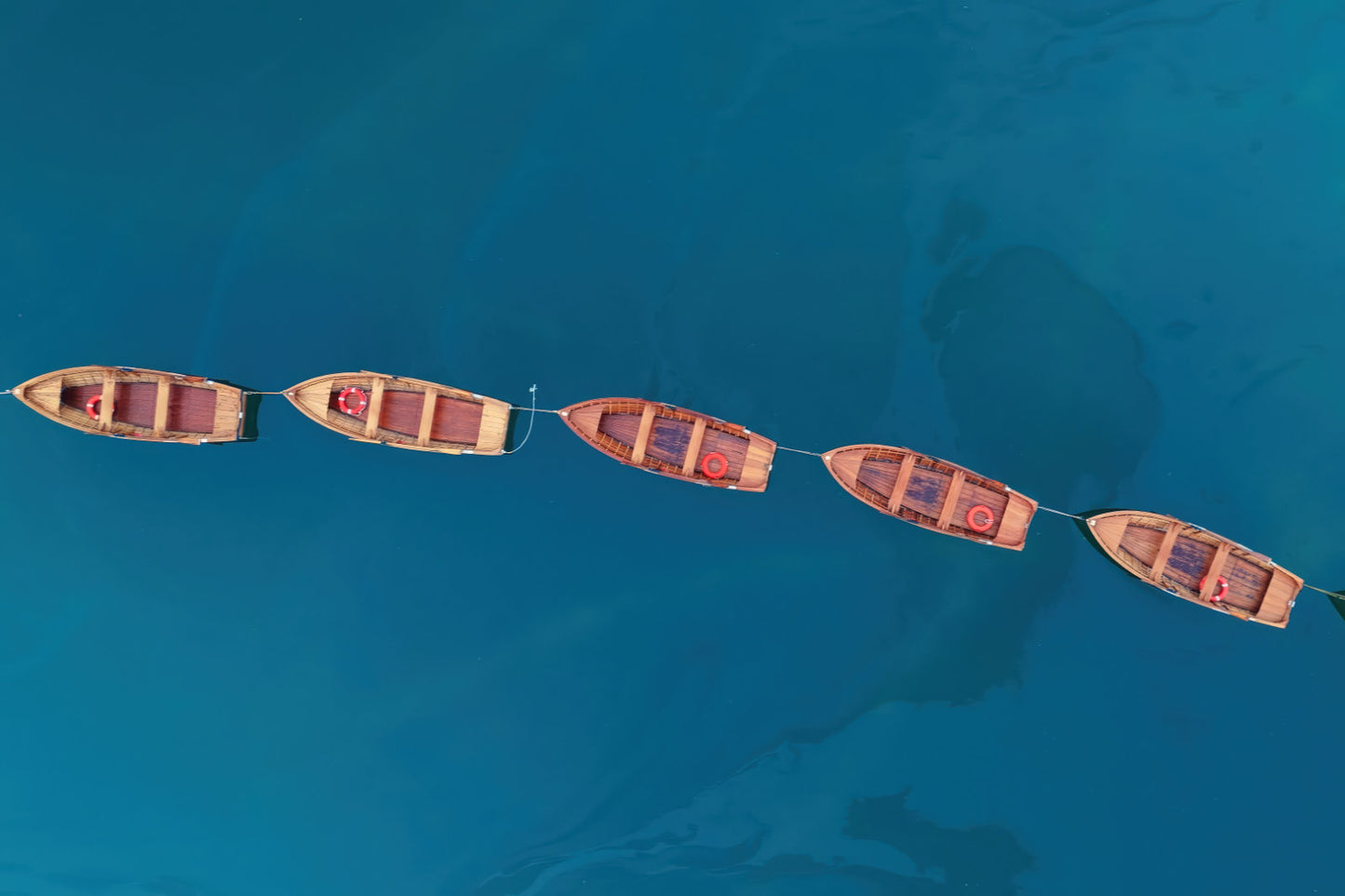Aerial view of five small wooden boats arranged in a line on clear turquoise blue water.