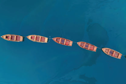 Aerial view of five small wooden boats arranged in a line on clear turquoise blue water.
