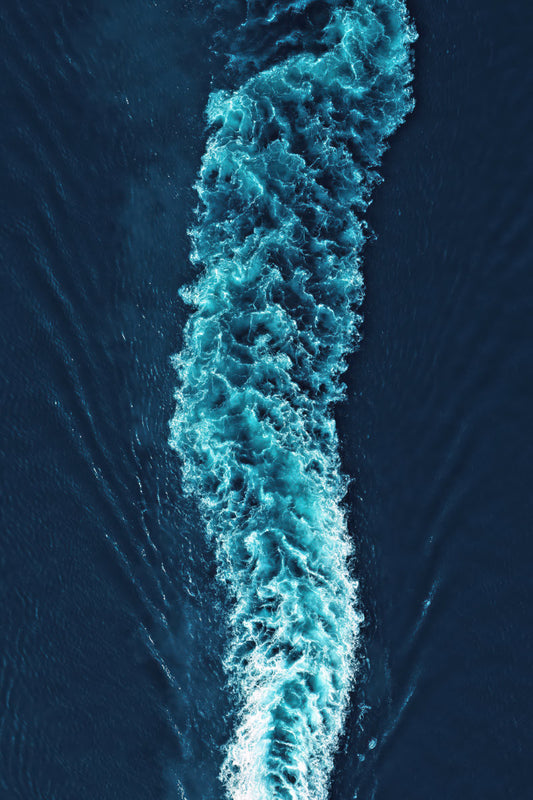 Aerial view of deep blue ocean water with a bright turquoise and white foaming wake running vertically through the center.
