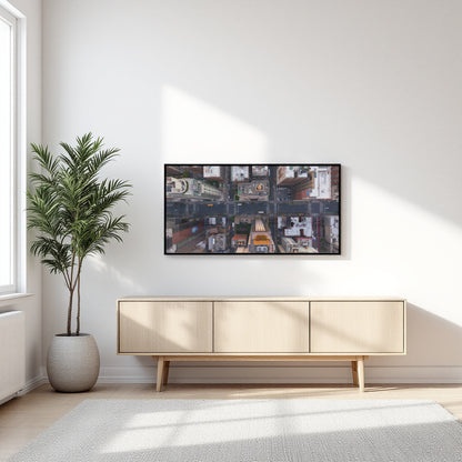 A framed wall art print showing a collage of street scenes, displayed above a light wood sideboard in a bright, modern room with a potted palm and window light.