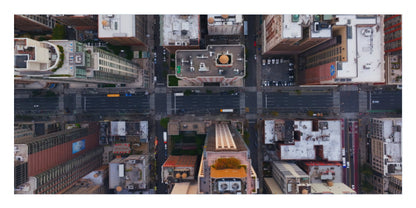 A top-down aerial photograph of a city street intersection with surrounding buildings and rooftops, shown as a square art print or poster.