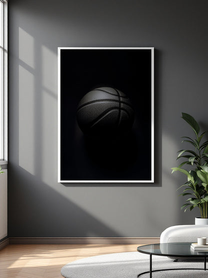 A framed wall art print featuring a dark basketball on a black background, hung on a gray wall in a modern living room setting with a plant and white sofa visible.