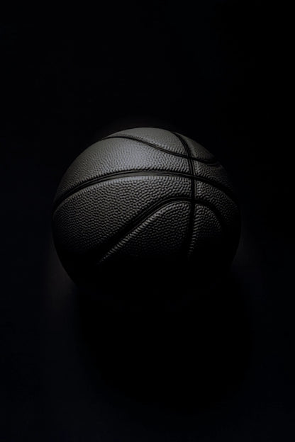 A black basketball with pebbled texture and dark painted seams, photographed against a very dark black background with dramatic low-key lighting.