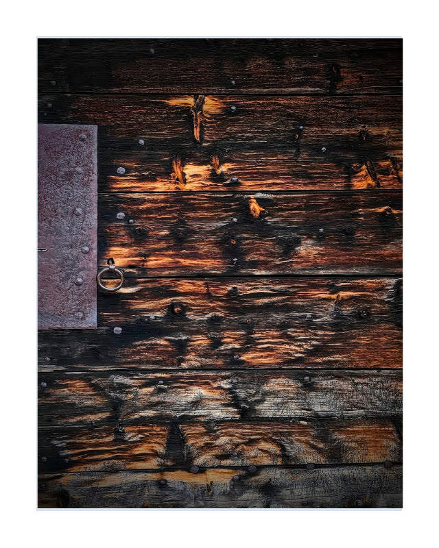A square art print or photo featuring a rustic dark wooden plank surface with weathered brown and black wood tones, warm orange highlights, metal nails, and a small metal ring on the left side, centered on a white background.