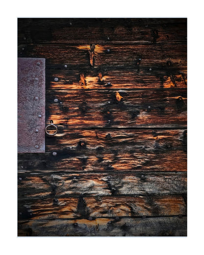 A square art print or photo featuring a rustic dark wooden plank surface with weathered brown and black wood tones, warm orange highlights, metal nails, and a small metal ring on the left side, centered on a white background.