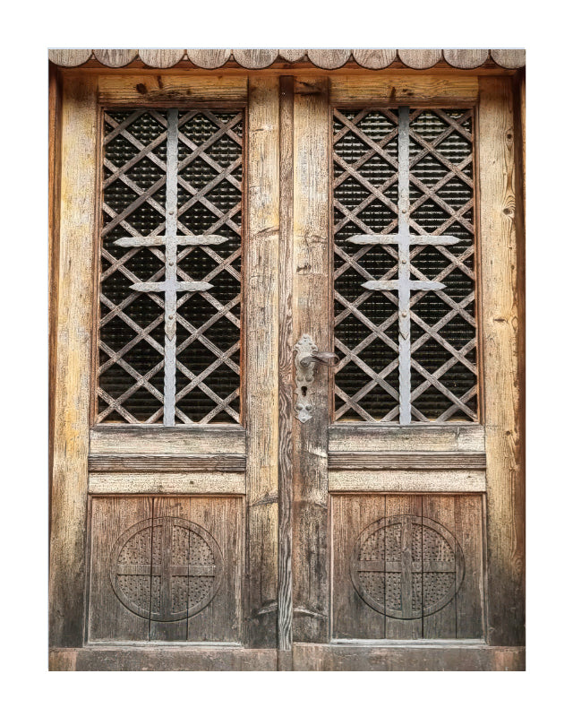 A pair of weathered wooden double doors with diamond-patterned lattice windows and carved circular details, shown against a plain white background.