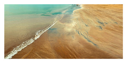 Aerial view of a beach shoreline with turquoise water on the left and warm sandy sand on the right, showing a long white surf line running diagonally across the frame.