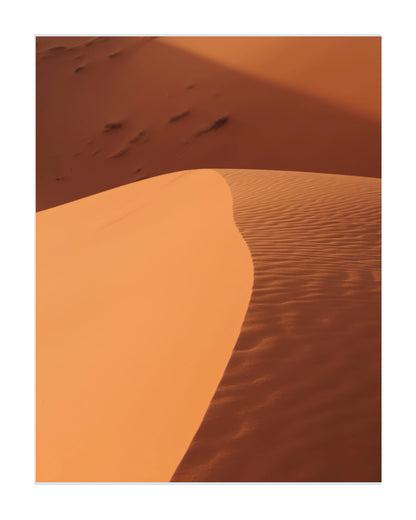 A minimalist art print depicting desert sand dunes in warm orange and brown tones, framed with a clean white border.