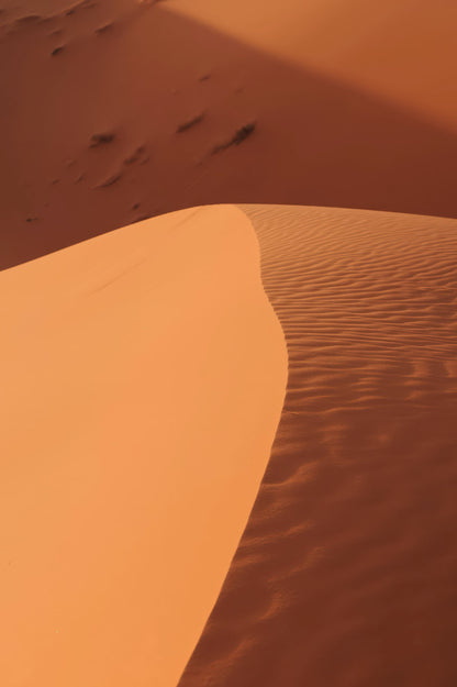 A close-up view of desert sand dunes in warm orange-brown tones, with rippled texture on one slope and smooth shading on the other.