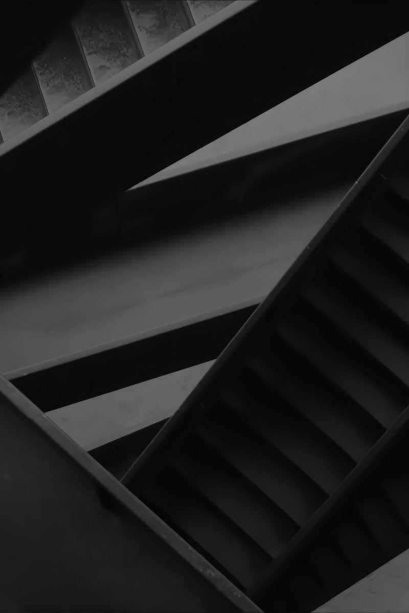 A dramatic black and white architectural photograph of concrete staircases, showing geometric lines and shadows.
