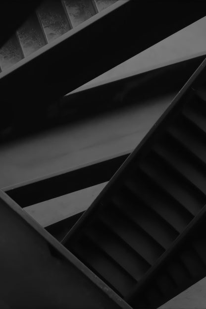 A dramatic black and white architectural photograph of concrete staircases, showing geometric lines and shadows.