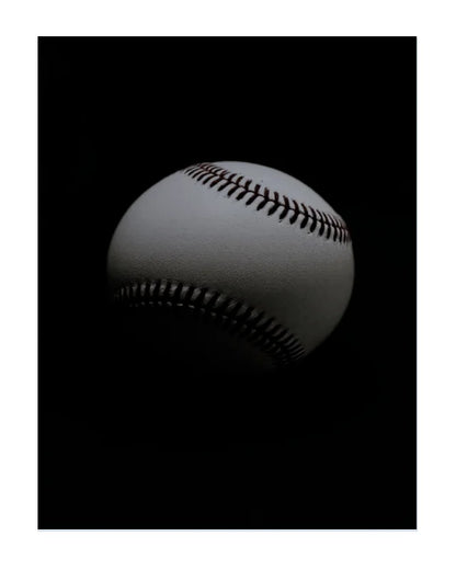 A single baseball photographed against a solid black background, with the ball itself appearing white to light gray and the visible stitching in dark brown/black.