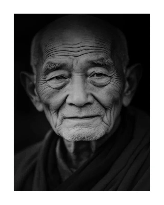 Black and white portrait print of an elderly Buddhist monk with deep wrinkles and a serene expression, wearing dark robes against a dark background.