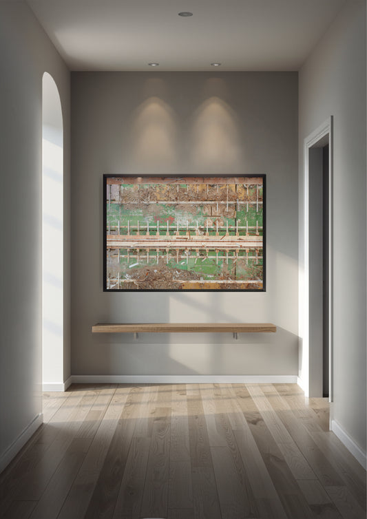 A framed abstract landscape art print with green, brown, and beige tones, displayed on a gray wall in a modern hallway with a light wood floating shelf below it.