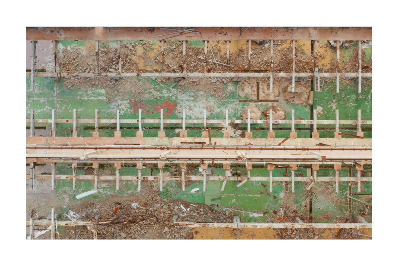 A close-up view of a weathered green and beige industrial wall and machinery panel with rusted metal, wooden beams, and debris.