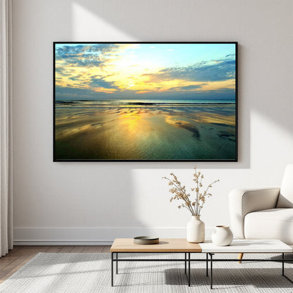 A framed landscape art print of a golden beach sunset hanging on a white wall in a modern living room setting with a coffee table and white sofa.