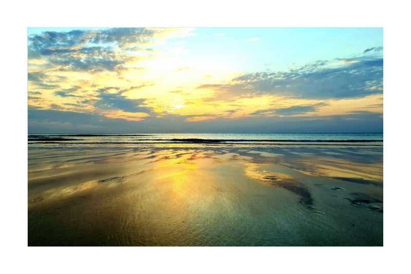 A scenic photograph of a beach at sunset, with golden light reflecting on wet sand and calm water under a blue and yellow sky.