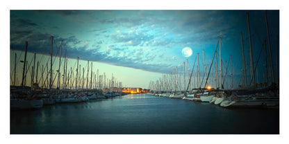 A scenic photograph of a marina at dusk or dawn under a full moon, with rows of sailboat masts lining a calm water channel and warm lights visible in the distance.