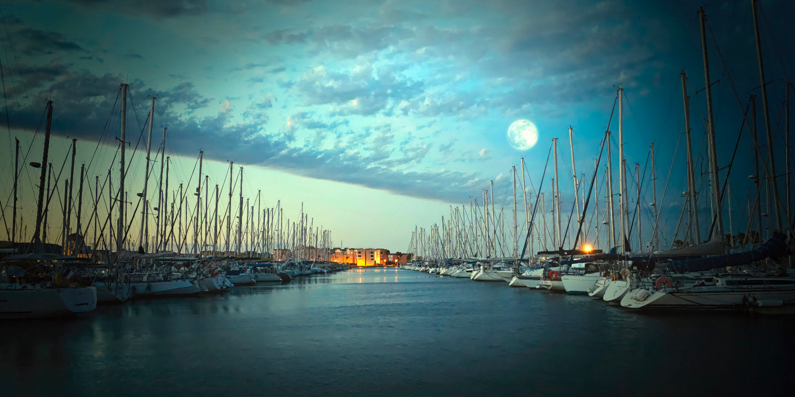 A scenic night harbor with rows of sailboats lined up under a cloudy sky, with a bright full moon visible in the distance above calm water.
