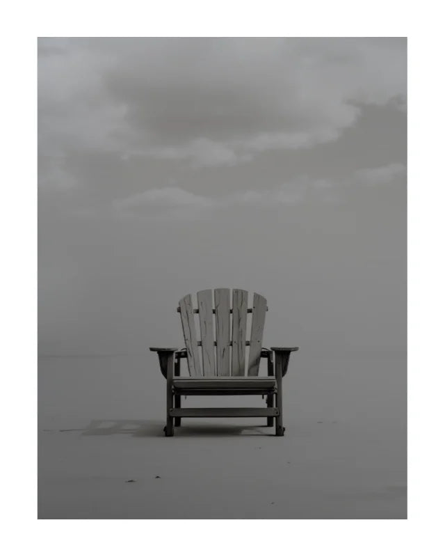 A single light-colored wooden Adirondack-style chair sits centered on a flat, misty gray surface under a cloudy overcast sky.