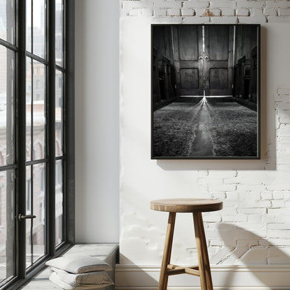 A black and white framed art print depicting a long hallway with a central staircase, displayed on a white brick wall above a wooden stool in a modern loft room setting.