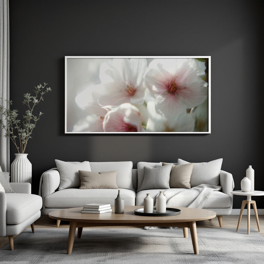 A large framed wall art print featuring soft white and pink flowers, displayed above a light gray sofa in a modern living room setting.