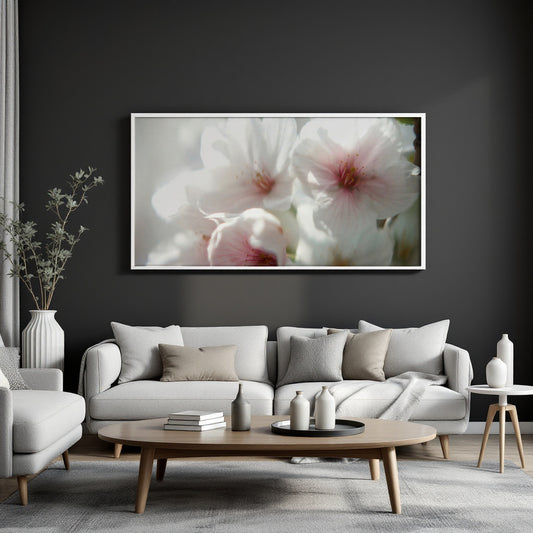 A large framed wall art print featuring soft white and pink flowers, displayed above a light gray sofa in a modern living room setting.