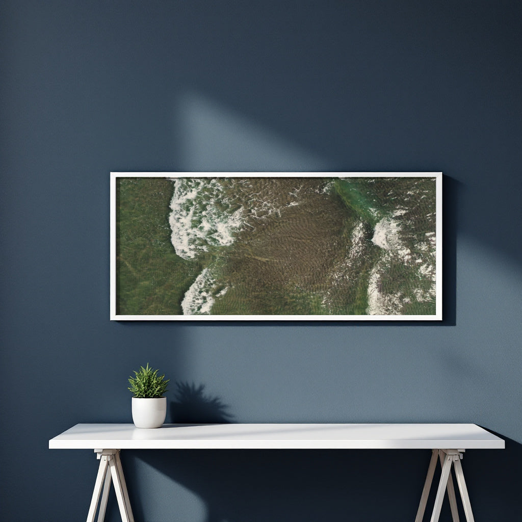 A framed aerial landscape photograph of green marshlands and white surf is displayed on a dark blue wall above a white console table with a small potted plant.