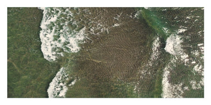 An aerial satellite-style photograph of a coastal area with green water, white surf, and a large brownish submerged or exposed reef/rock formation in the center.