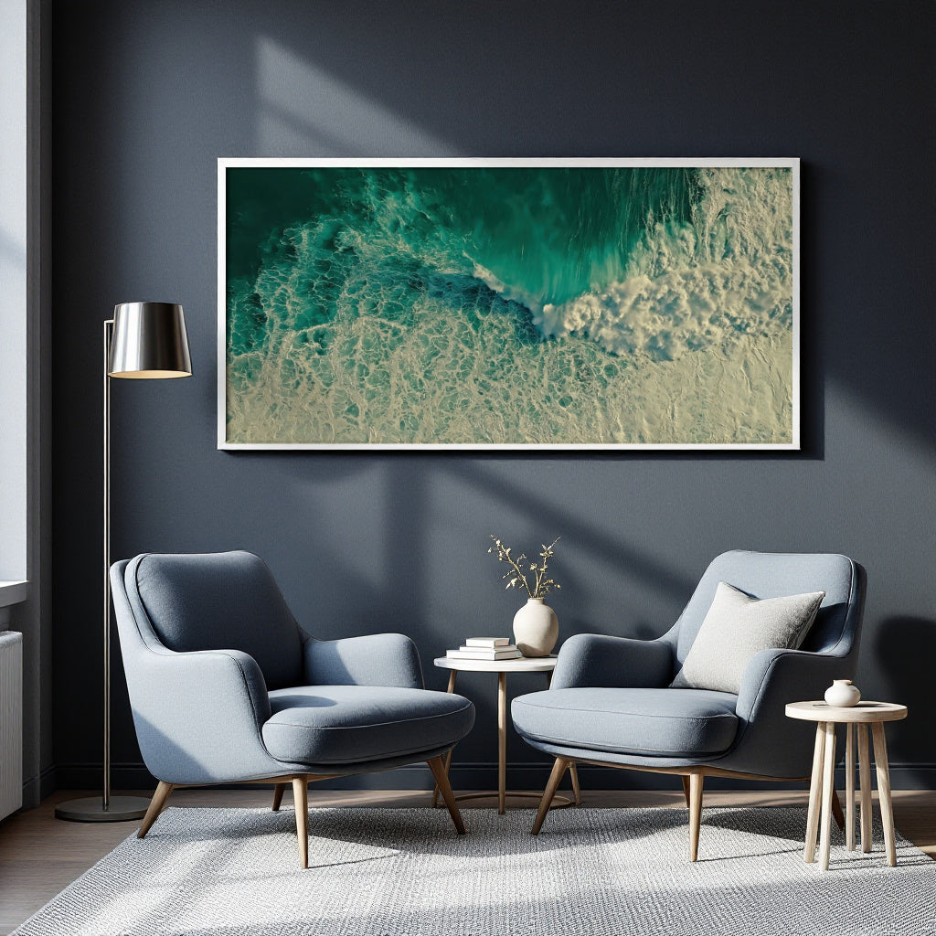 A large framed abstract art print depicting turquoise and beige ocean waves, displayed on a dark gray wall in a modern living room setting with two blue armchairs, a floor lamp, and a side table.