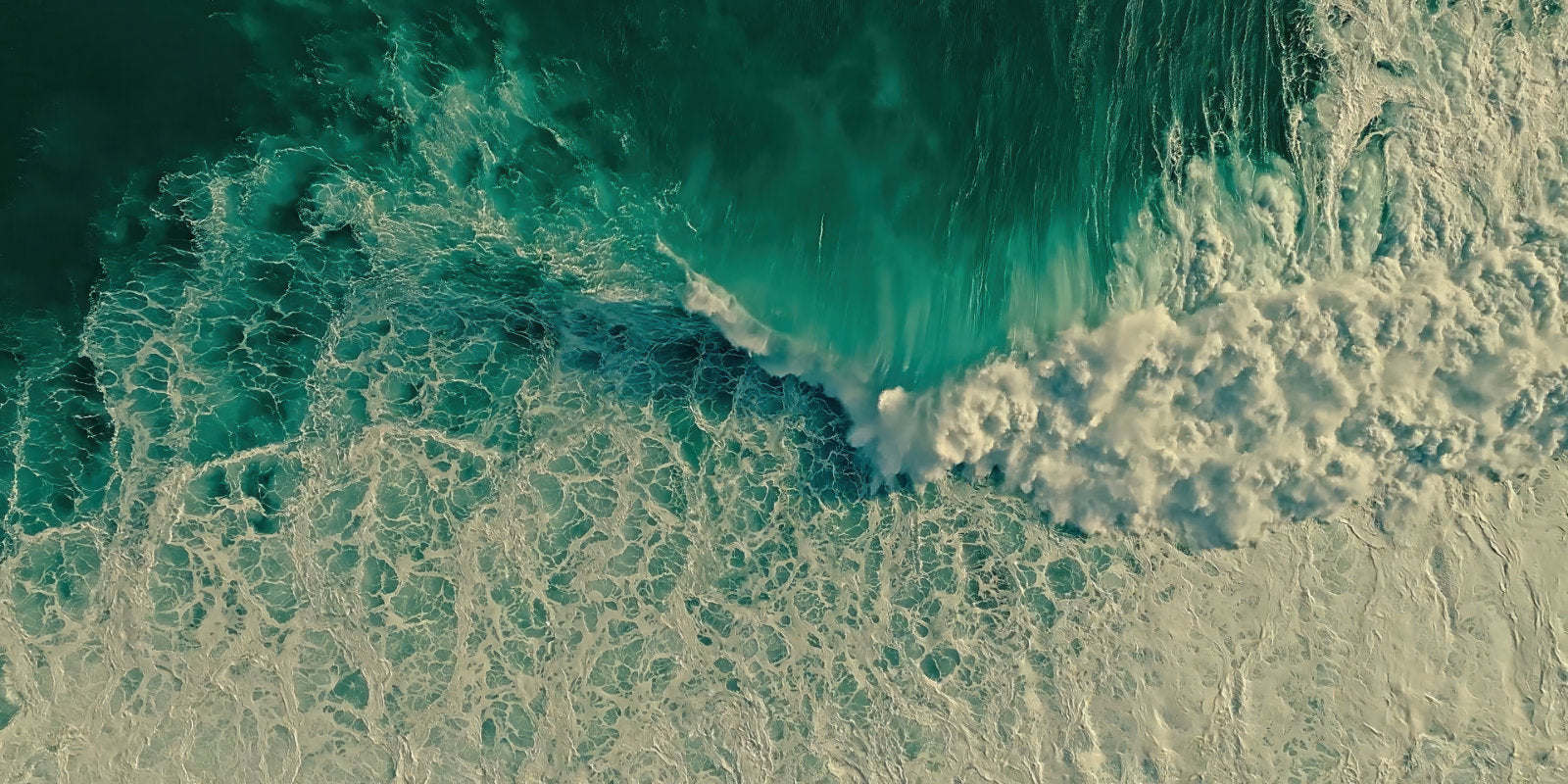 Aerial view of turquoise ocean waves breaking with white foam on a sandy shore.
