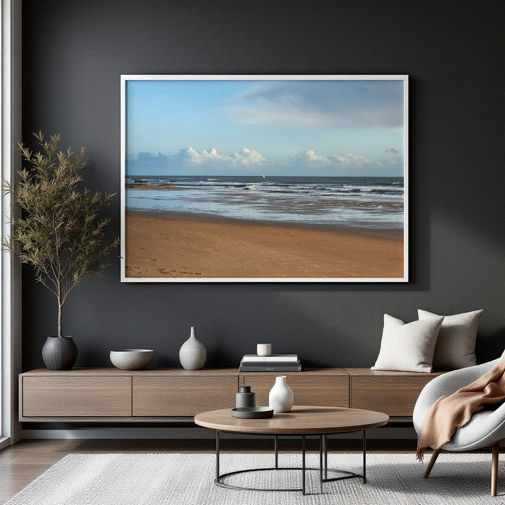 A framed beach landscape print hangs on a dark charcoal wall above a modern wooden console table in a styled living room. The print depicts a sandy beach, ocean waves, and a blue sky with clouds, surrounded by a white frame.