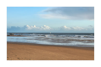 A scenic photograph of a sandy beach with gentle ocean waves under a blue sky with scattered white clouds.