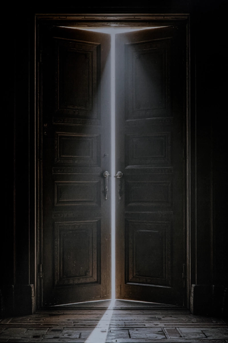 Dark double wooden doors opening into a brightly lit room, with a beam of light shining down the center onto a worn wooden floor.